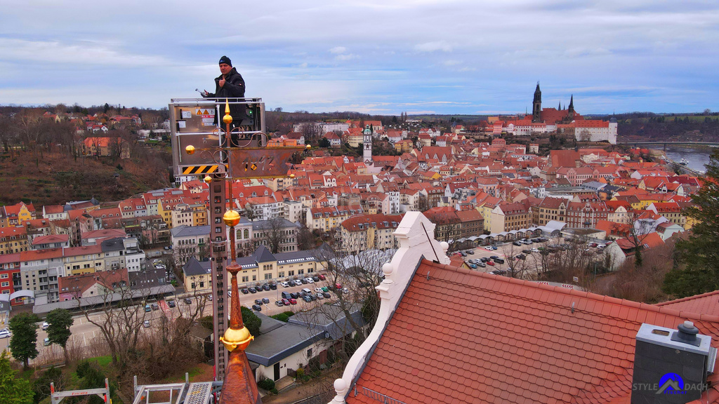 Dachdecker Mirko Fischer aus Colditz steht im Hubsteiger und installiert vergoldete Wetterfahne über den Dächern der Stadt Meißen. Im Hintergrund sieht man den Dom und die Elbe