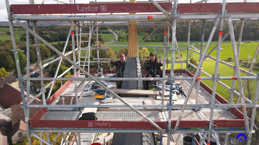 Foto zeigt Schieferdecker Mirko Fischer und Azubi Justin Härtel alias Schiefer Henry auf 38m Höhe auf dem Gerüst an der Heilig Kreuz Kirche in Diefenbach. Die beiden Dachdecker decken Schiefer